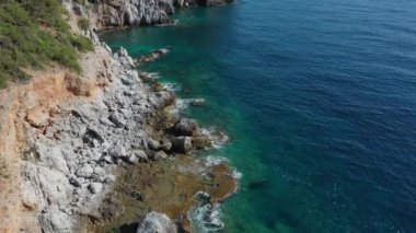 Dalgaların mavi okyanustaki Alanya Hindi kıyısındaki kayalıklardaki uçurumlara düşüşünü gösteren hava manzarası. Yeşil doğa ve okyanusun hava aracı fotoğrafçılığı