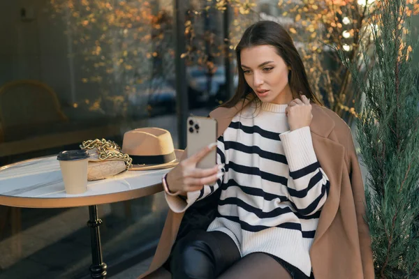 穿着休闲装的快乐女人面带微笑 喝咖啡 上网聊天 独自一人用手机自拍 — 图库照片