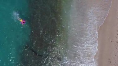 Temiz suyla dolu güzel bir okyanusun üzerinde şişme bir halka üzerinde yüzen genç bir adamın havadan görüntüsü. Tatilin tadını çıkaran adam yazın dinleniyor..