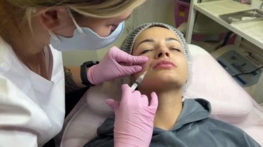 Güzellik kliniğinde çalışan güzel bir kadın. Doldurucu enjeksiyon. Mor eldivenli doktor burun kıvrımında iğne yapıyor.