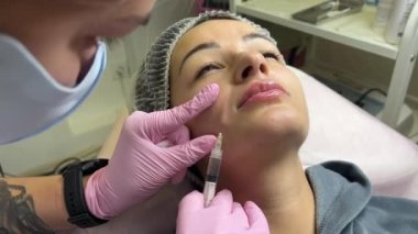 Güzellik kliniğinde çalışan güzel bir kadın. Doldurucu enjeksiyon. Mor eldivenli doktor burun kıvrımında iğne yapıyor.