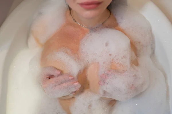 A sexy girl takes a bath. Large beautiful female breasts in bath foam.