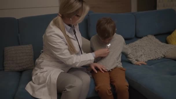 家族の医者が家で少年を検査する 小児科医の女の子は子供を扱う — ストック動画