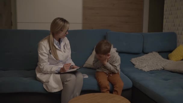 家族の医者が家で少年を検査する 小児科医の女の子は子供を扱う — ストック動画