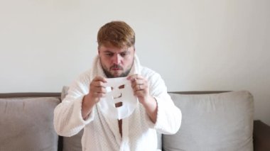 Funny man having fun at home using the face mask for better mood feeling awesome. Portrait of guy doing cosmetic procedures. People skin care concept.