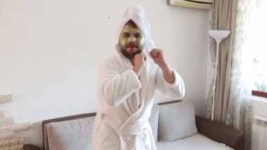 Komik, mutlu adam evinde tek başına dans ediyor. Neşeli hissediyor ve çılgın danslar yapıyor. Nemlendirici kırışıklık önleyici maskeli bir erkek yüzü. İnsan ve cilt bakımı kavramı. 