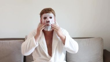 Funny man having fun at home using the face mask for better mood feeling awesome. Portrait of guy doing cosmetic procedures. People skin care concept.