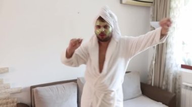 Komik, mutlu adam evinde tek başına dans ediyor. Neşeli hissediyor ve çılgın danslar yapıyor. Nemlendirici kırışıklık önleyici maskeli bir erkek yüzü. İnsan ve cilt bakımı kavramı. 