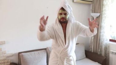Komik, mutlu adam evinde tek başına dans ediyor. Neşeli hissediyor ve çılgın danslar yapıyor. Nemlendirici kırışıklık önleyici maskeli bir erkek yüzü. İnsan ve cilt bakımı kavramı. 