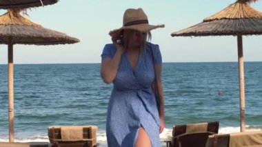 Uzun mavi elbiseli, uzun sarı saçlı güzel genç bir kadın kumsal boyunca yürüyor. Mavi elbiseli kız. Rüzgarda dalgalanan uzun kırmızı elbise.. 