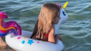 Happy baby girl swimming on an inflatable swimming unicorn in the sea. 