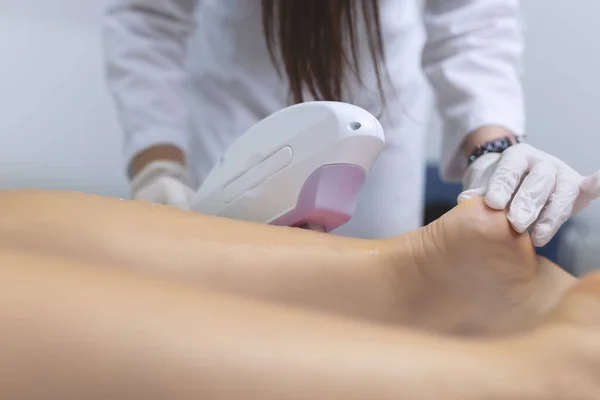 Beautician removes hair on beautiful female legs using a laser.