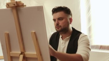 Evdeki oturma odasında tuvale resim yapan çekici bir adam. Hobi ve eğlence konsepti