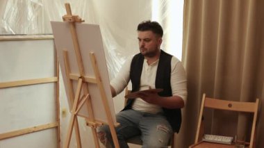 Evdeki oturma odasında tuvale resim yapan çekici bir adam. Hobi ve eğlence konsepti