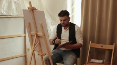 Evdeki oturma odasında tuvale resim yapan çekici bir adam. Hobi ve eğlence konsepti