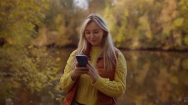 Gülümseyen sarışın kadın mesaj yazıyor ya da akıllı telefonda internet kullanıyor. Sonbaharda açık havada güzel bir kız. 