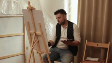 Evdeki oturma odasında tuvale resim yapan çekici bir adam. Hobi ve eğlence konsepti