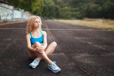 Genç, kıvırcık, atletik yapılı bir sarışın stadyumda antrenmandan önce ısınma turu yapıyor. Açık hava sporları. 