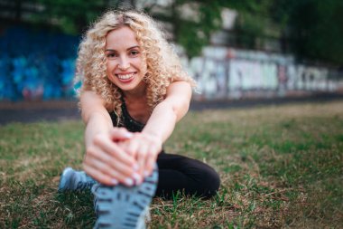 Genç, kıvırcık, atletik yapılı bir sarışın stadyumda antrenmandan önce ısınma turu yapıyor. Açık hava sporları. 