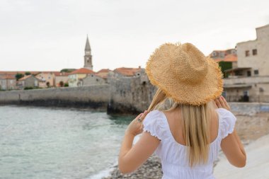 Hasır şapkalı beyaz kadın, Karadağ 'ın Budva kentindeki gözlem güvertesinde dikiliyor.