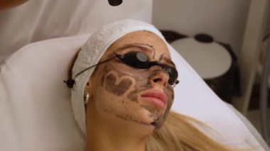 Güzellik uzmanları, güzellik salonundaki bir kanepede uzanan gözlüklü güzel bir müşteriye karbon soyuyorlar. Yüz temizleme konsepti. Kozmetik Hizmetleri. 