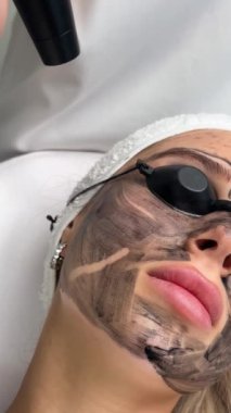 Güzellik salonundaki kanepede uzanan güvenlik gözlüğü başlıklı genç ve güzel bir müşteri tarafından el yapımı donanım karbonu. Yüz temizleme konsepti. Kozmetoloji Servisi