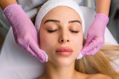 Güzellik uzmanları kozmetoloji ameliyatından sonra kadının yüzünü peçeteyle siliyorlar. Kozmetik prosedürü. Spa tedavisi konsepti. Yüz bakımı, kozmetoloji