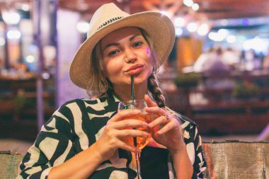 Yaz tatilindeki kadın turist gece plaj barında kokteyl içiyor.