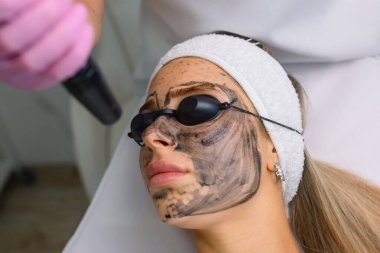 Güzellik salonundaki kanepede uzanan güvenlik gözlüğü başlıklı genç ve güzel bir müşteri tarafından el yapımı donanım karbonu. Yüz temizleme konsepti. Kozmetoloji Servisi