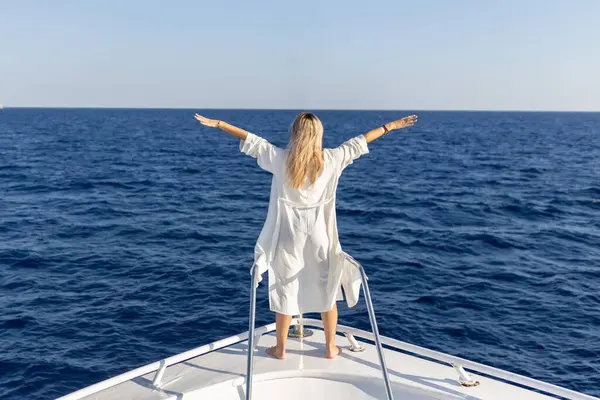 Beyaz elbiseli zarif seksi kadın parmaklıkların yanında duruyor ve gün batımını seyrediyor. Yat tarzı gibi. Yüksek kalite fotoğraf