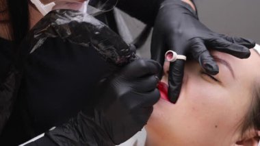 Kozmetik uzmanı bir kadının yüzüne kalıcı makyaj yapıyor. Uzman, hastaların dudaklarına yakın plan dövme uygular.. 