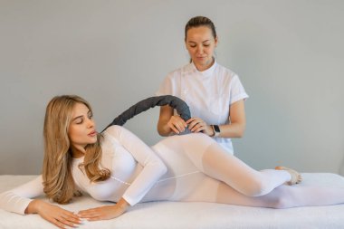 Beyaz takım elbiseli bir kadın spa salonunda selülit karşıtı masaj yaptırıyor. LPG ve vücut şekillendirme tedavisi klinikte. Vücut ağırlığını LPG masajıyla sıfırlayın.. 