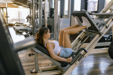 Güzel kadın sportif kız spor salonunda bacak presi makinesi kullanıyor..