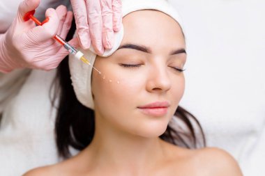 Kozmetik uzmanı güzel bir kadının yüzüne kırışıklık önleyici iğneler yapıyor. Güzellik salonunda kadın estetiği.