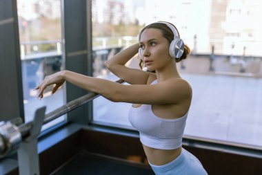 Spor kıyafetleri giyen seksi kız fitness merkezinde bir sonraki demirci makinesine poz veriyor. Yüksek kalite fotoğraf