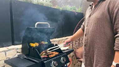 Gaz barbeküsünde ızgara et şişleri, sosisler ve mısır. Dışarıda yemek pişirirken ızgaradan duman yükselir. Piknik ya da arka bahçe partisi için lezzetli yaz yemeği hazırlığı