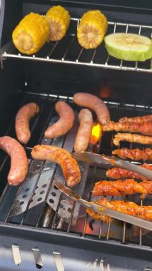 Gaz barbeküsünde ızgara et şişleri, sosisler ve mısır. Dışarıda yemek pişirirken ızgaradan duman yükselir. Piknik ya da arka bahçe partisi için lezzetli yaz yemeği hazırlığı