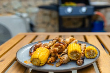 Izgara sosis, şiş ve mısır bir tabakta sebzeli ve yassı ekmekli mangalın yanında. Lezzetli ızgara yemekli açık hava yemek sahnesi. Yüksek kalite fotoğraf