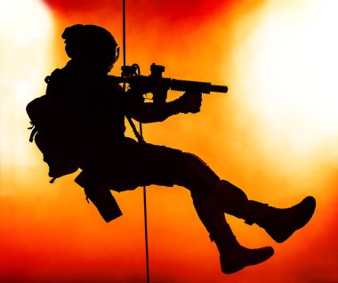 Silhouette of police officer in tactical gear descending from a height, rope exercises with weapons. Tactical rappelling, anti-terror or counter terrorism operation in darkness in rappelling harness