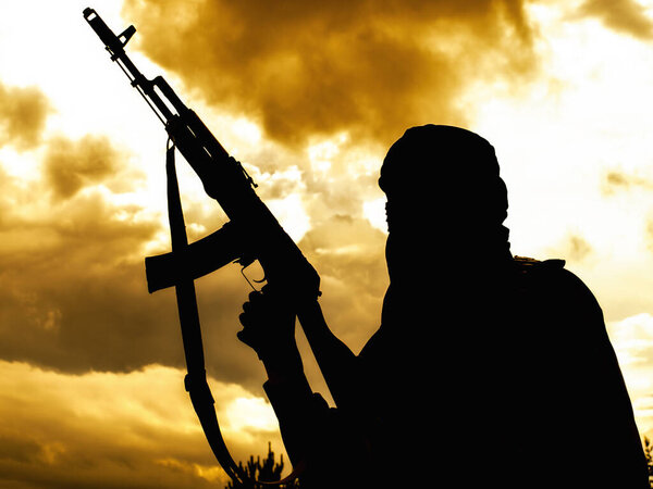 Muslim militant with rifle in the desert on sunset uder heavy clouds