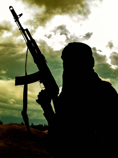 Muslim militant with rifle in the desert on sunset or dusk