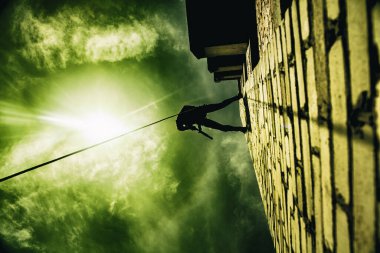 Silhouette of police officer in tactical gear descending from a height, rope exercises with weapons. Tactical rappelling, anti-terror or counter terrorism operation in darkness in rappelling harness
