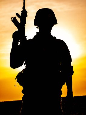 Gün batımında tüfekli Amerikan askerinin silueti arka planda güneş batarken ayakta duruyor.