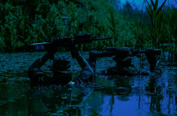 士兵们在沼泽地的中心活动 被淹没在沼泽地的水域里 只有武器和来复枪 这是特种部队夜间隐蔽作战的极端条件 图库图片