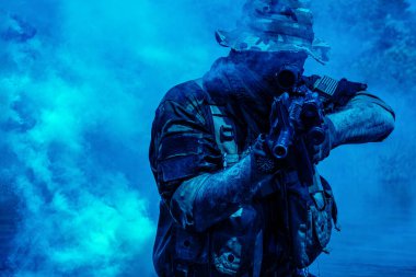 Mavi dumanın ortasında, dinamik ve yoğun bir sahnede, tüfekli ve taktik teçhizatlı, kamuflajlı asker..