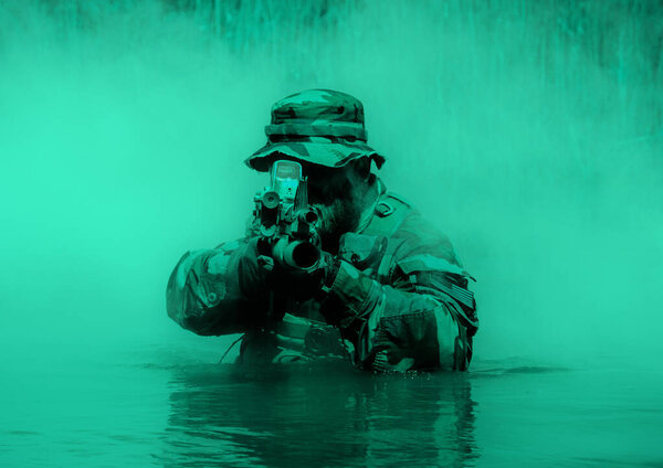 Soldier in a camouflage uniform and hat aiming a rifle while half-submerged in water, with a background of green mist.
