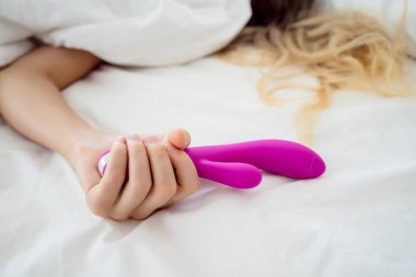 Yatakta elinde yetişkinler için bir seks oyuncağı tutan genç seksi kadın..