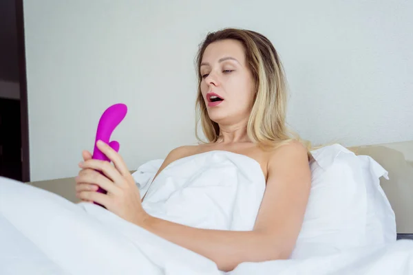 stock image Young sexy woman in the bed holding in her hands a sex toy for adults.