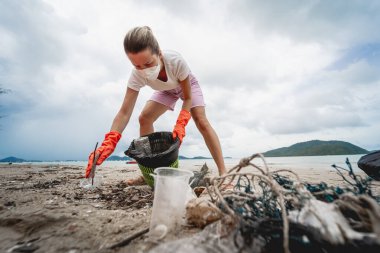 A female ecologist volunteer cleans the beach on the seashore from plastic and other waste.