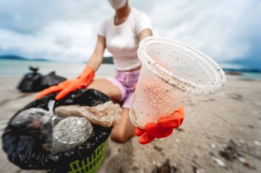 A female ecologist volunteer cleans the beach on the seashore from plastic and other waste.